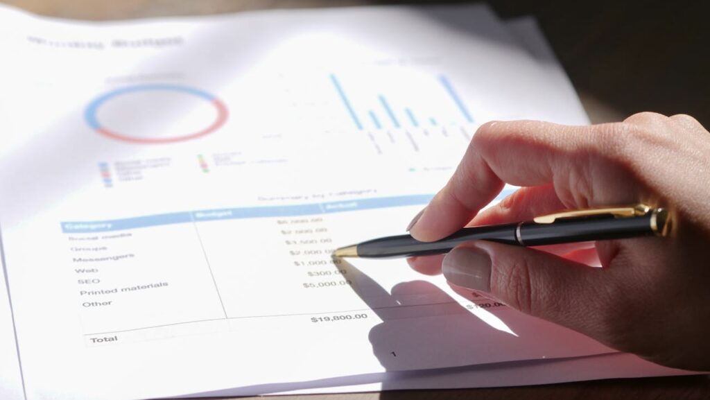 pexels photo 7054415 Hand holding pen, analyzing budget with charts and graph paper.